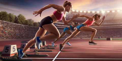 Female athletes sprinting. Three women in sport clothes run at the running track in professional...