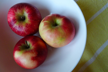 three red and yellow juicy apples from autumn harvest placed in a bowl on a kithchen table, healthy snack during diet or healthy eating concept