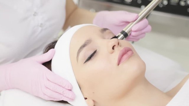 Young Woman Visiting Beauty Salon. Getting Anti-Aging Procedure. Beautician Making Facial Rejuvenation. Concept of Mesoporation. Enjoying No-Needle Mesotherapy.