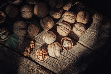 Walnut kernels and whole walnuts on rustic old wooden table in spots of sunlight.
