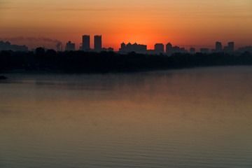 Silhouette of a city buildings on a horizont in a rays of red rising sun over Dneper, Kyiv, Ukraine