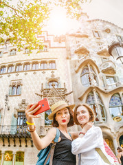 Obraz na płótnie Canvas Portrait of two female tourist friends hugging in front of the architecture of the Casa Batllo in Barcelona