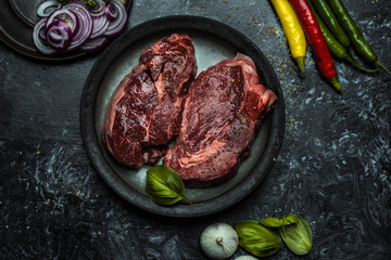 on a dark background fresh, red, raw beef and spilled coarse salt, next to it lies fresh vegetables