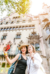 Portrait of two female tourist friends hugging in front of the architecture of the Casa Batllo in Barcelona