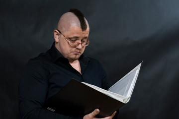 Punk reading a working folder. Black shirt. Iroquois. Glasses. Sight attentive and serious.