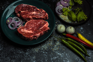 on a dark background fresh, red, raw beef and spilled coarse salt, next to it lies fresh vegetables