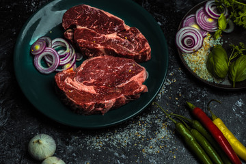 on a dark background fresh, red, raw beef and spilled coarse salt, next to it lies fresh vegetables