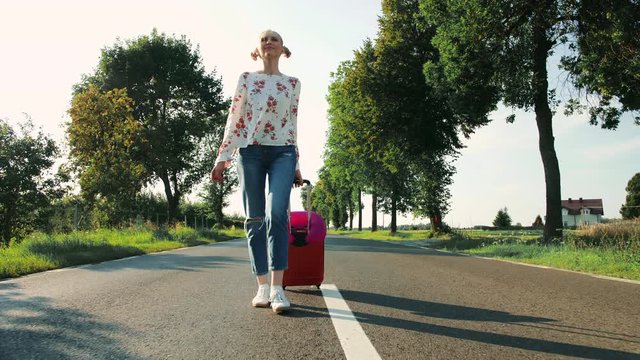 Cheerful Young lady with suitcase walking on road.