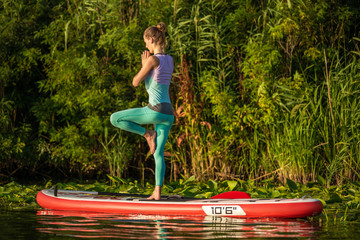 Young woman are doing yoga on a stand up paddle board SUP on a beautiful lake or river
