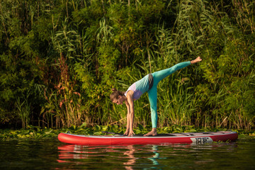 Photo of young woman doing hand stand on stand up paddle board. She wearing a leggings and top.