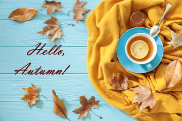 Autumn background concept - blue cup of black tea with lemon slice and honey on a yellow scarf, dried leaves and text Hello, Autumn on a blue wooden background.