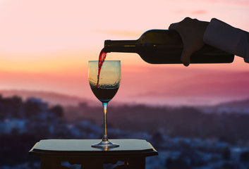 Female hand with bottle pours red wine into glasses on blurred San Francisco city background....