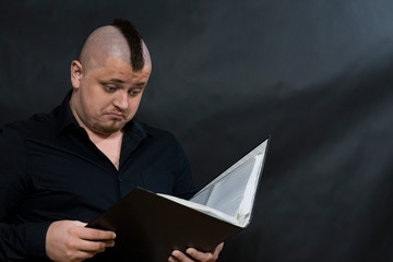 Punk reading a working folder. Black shirt. Iroquois. Sight attentive and surprised.