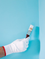 Image of man holding paintbrush in front of blue wall.