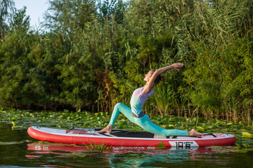 Young woman are doing yoga on a stand up paddle board SUP on a beautiful lake or river