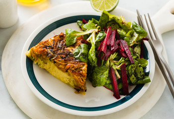 savory salty  Upside-Down pie from white cabbage, carrots and onions. gluten free no eggs , with chickpea flour. family breakfast or party snack on a white marble table with salad from greens and beet