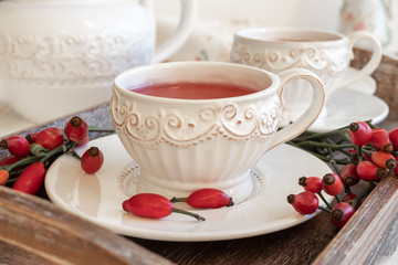 Rose hip tea in a white cup with fresh rose hips