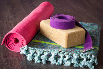 Yoga studio props selection on wooden floor. Pink mat, cork brick, purple belt and colorful cotton...
