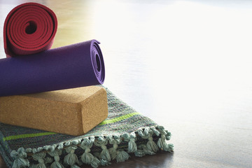 Yoga props selection in balance. Folded cotton mat, cork block and colorful rolled mats on studio...