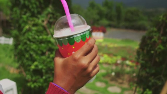 Close up girl drinking from the paper cup by strow in lush garden