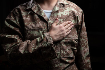 Young soldier with hand on heart standing on black background