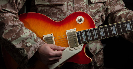 Young man in military uniform playing guitar, close up view, dark background