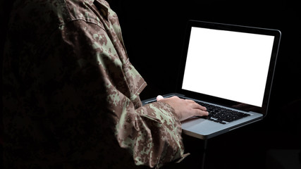 Young soldier working with a laptop computer with blank screen on black background