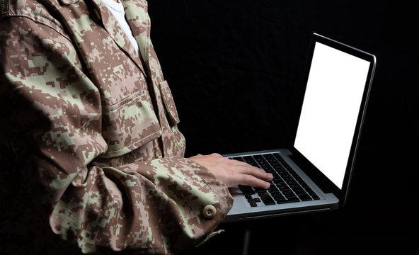 Young soldier working with a laptop computer with blank screen on black background