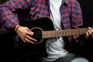 Fototapeta na wymiar Young man playing guitar, close up view, dark background
