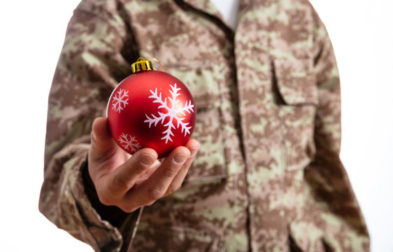 Young soldier holding a red christmas ball standing on white background