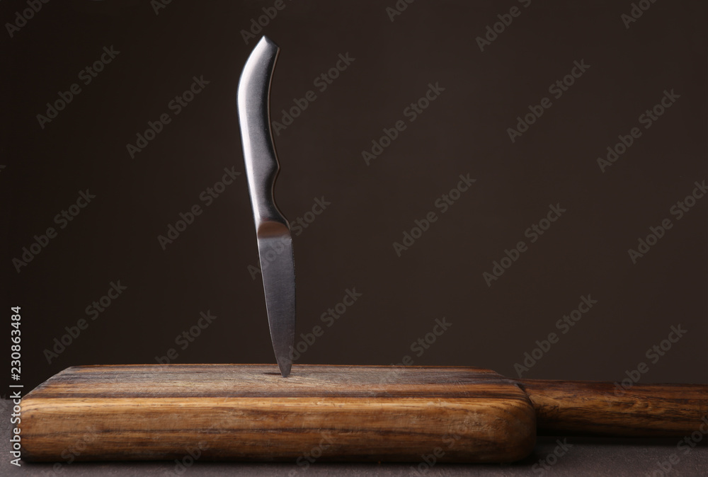 Wall mural Knife stuck in cutting board on dark background. Wood cutting board and kitchen knife against dark brown wall with copy space.