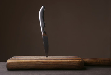 Knife stuck in cutting board on dark background. Wood cutting board and kitchen knife against dark...
