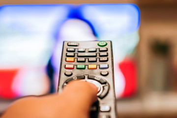 A hand pressing a television remote control button