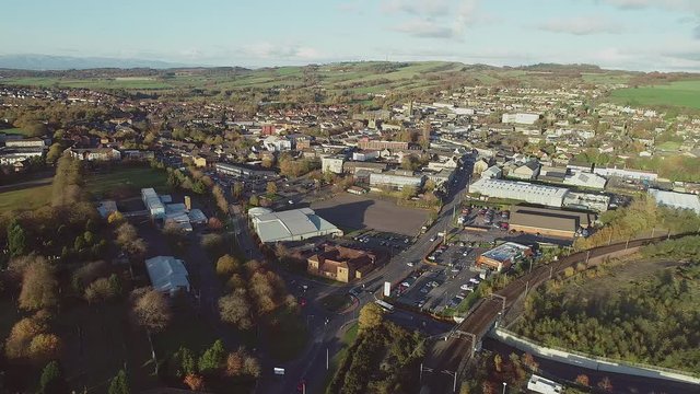 Aerial footage over the town of Bathgate in West Lothian, Scotland. Flying left. Passenger train arriving at Bathgate railway station.