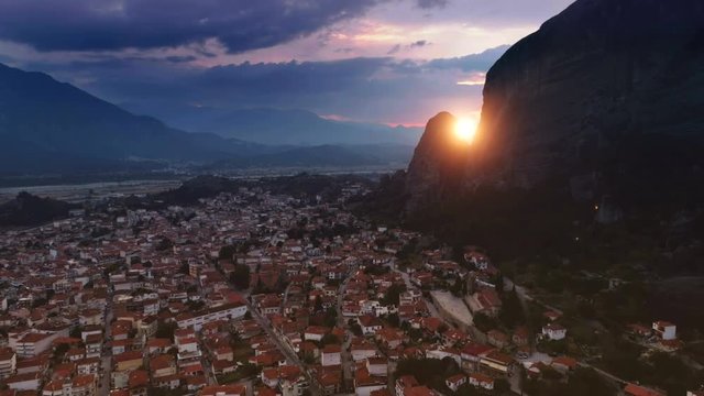Shooting from helicopter amazing valley at sunset dark blue sky and yellow big sun aerial shot historical place mountain Meteora surrounded by old city or town or suburb Kalambaka