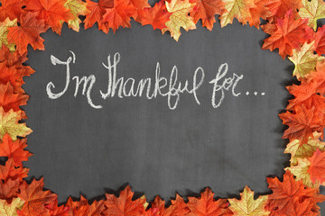 "I'm thankful for..."  message written on a blackboard framed with colorful autumn maple leaves