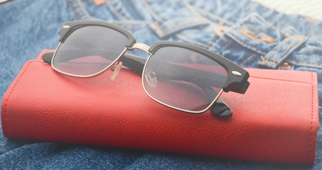 Women's things and accessories. Classic sunglasses, red leather purse, jeans.