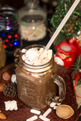 Mug of hot chocolate drink with marshmallow candies on top and lights on Christmas tree and decorations.