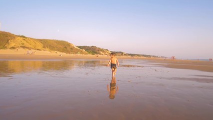 Slow motion - A child 3-5 years old running freely while the camera chase him and he laughs, in a sunny day in the beach 