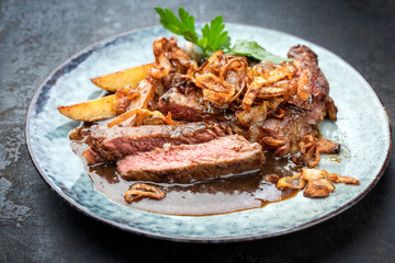 Traditional dry aged sliced roast beef with fried onion rings and potato chips as closeup on a plate with brown sauce