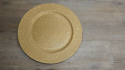 Fototapeta na wymiar Golden glistening plate, isoled on wooden background. Top view