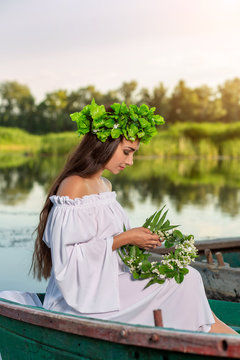 The nymph with long dark hair in a white vintage dress sitting in a boat in the middle of the river.