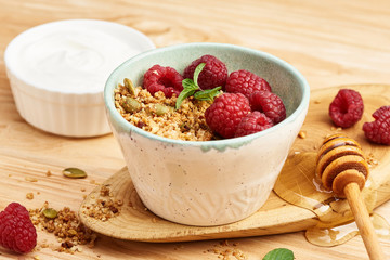 Homemade granola and yogurt in a bowl with raspberries on a wooden table.