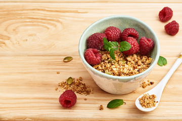 Homemade granola in a bowl with raspberries on a wooden table.