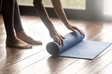 Equipment for sport training session concept. Girl wearing grey sporty pants rolling fitness mat...