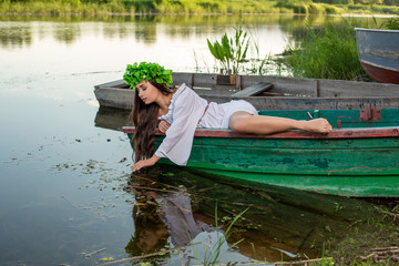 The nymph with long dark hair in a white vintage dress sitting in a boat in the middle of the river.