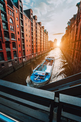 Touristic cruise boat in narrow canal of famous Speicherstadt warehouse district with red brick...