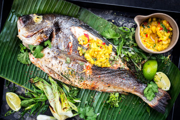 Fresh barbecue gilthead seabream with lettuce and mango chutney as top view on a green banana leaf