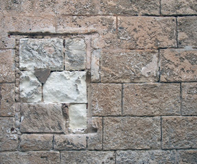 old stone wall built of large rough textured brown blocks with a repaired blocked up window