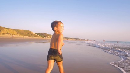 Slow motion - A child 3 years old running freely while the camera chase him and he laughs, in a sunny day in the beach 